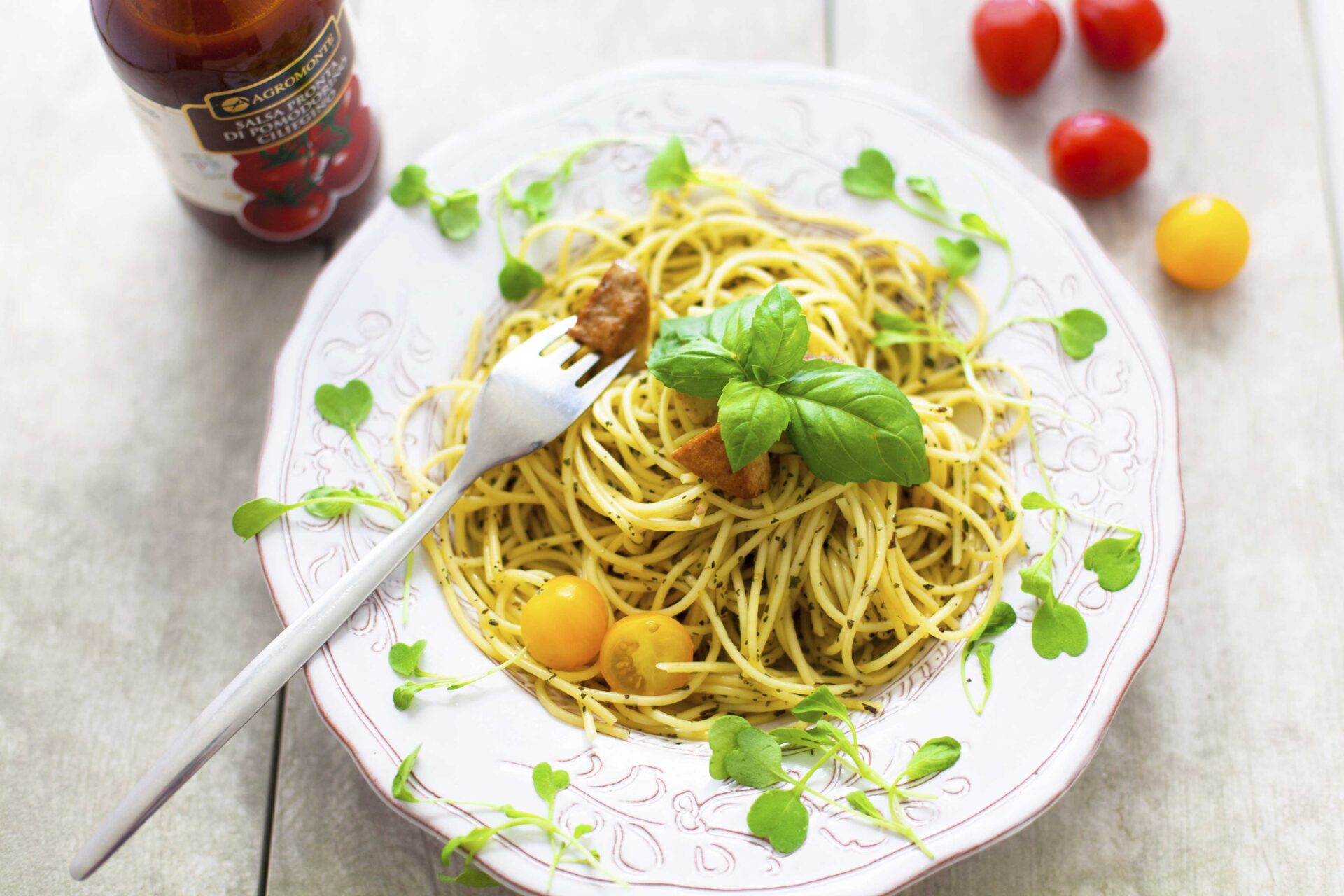 Spagettia pestokastikkeella ja kylmäsavutofulla tomaattien kera lautasella tarjoiltuna.