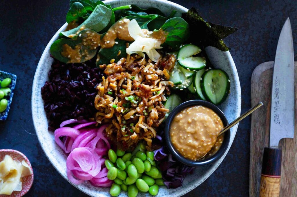 Värikäs sushi bowl eli sushikulho, jonka pohjalla on riisiä ja päällä kurkkua, edamamepapuja, marinoitua punasipulia ja rapeaksi paahdettua tofua sekä seesamikastiketta.