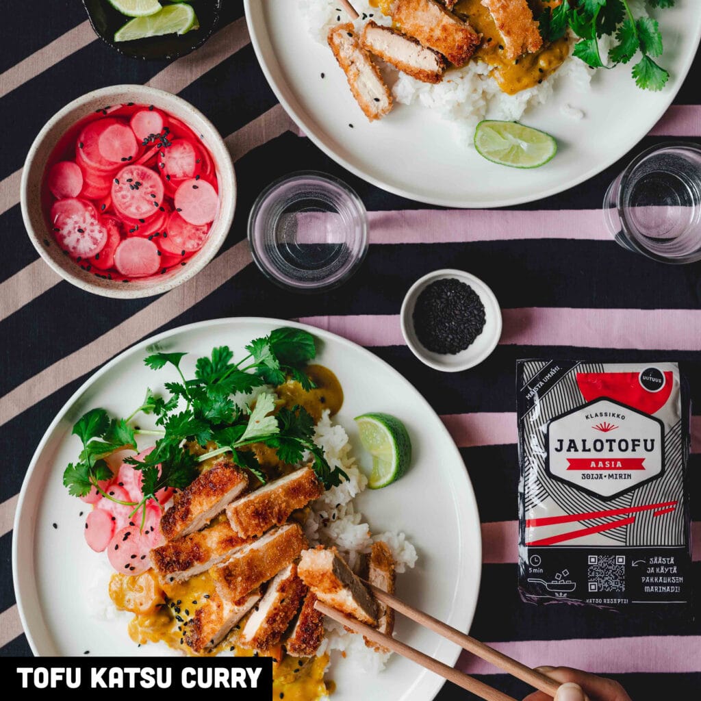 Tofu katsu curry annoksessa lautasella leikattuja, kanassiivujen näköisiä rapeita tofupaloja, vierellä Jalotofu-Aasia pakkaus ja marinoitua retiisiä. 