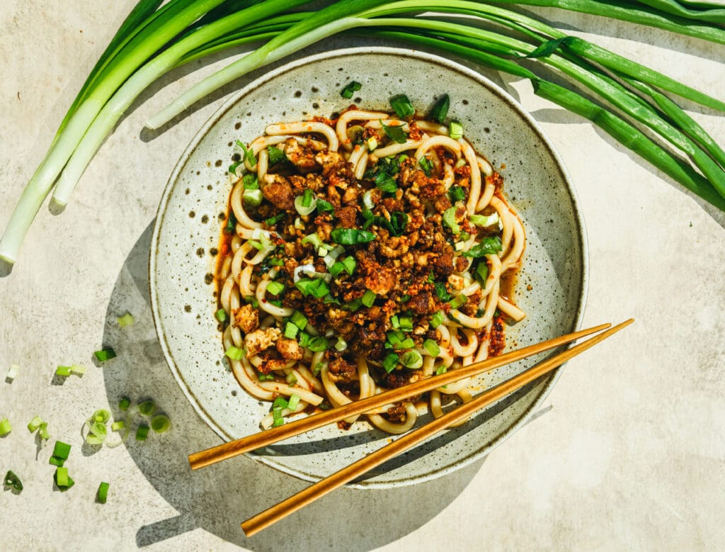 Muhkeat bulgogi-nuudelit rapealla tofulla lautasella, jonka vierellä on kevätsipulia.
