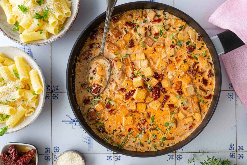 Maukas marry me tofu-kastike pannulla ja parmesaanilla maustettua pastaa kulhoissa.