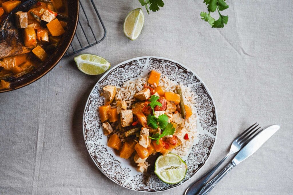 Lämmittävä uunicurry tofulla ja kurpitsalla lautasella riisin ja limesiivujen kanssa tarjoiltuna.