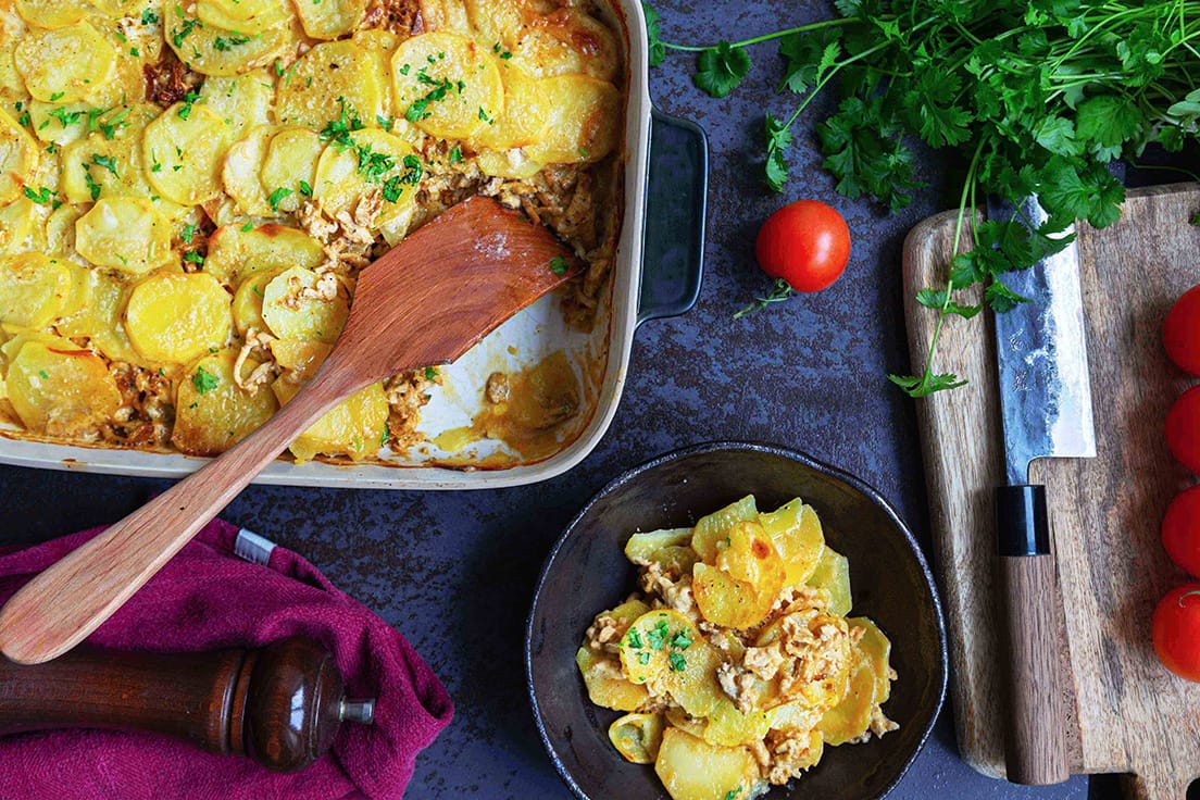Täyteläinen tofu-perunalaatikko vuoassa ja lautasella, näyttää samalta kuin perinteinen liha-perunalaatikko.